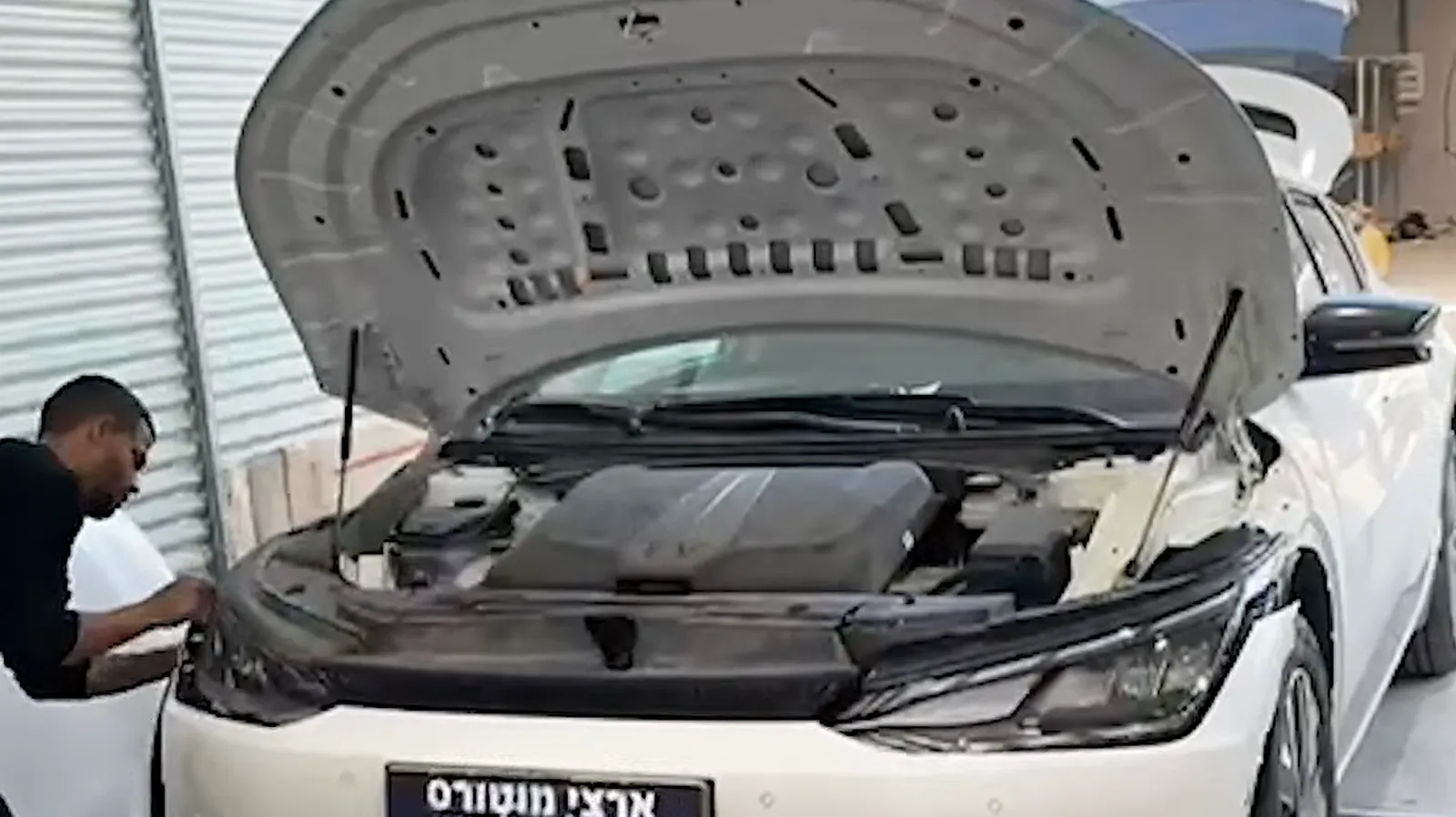 מכונאי של ארצי מוטורס עובד מתחת למכסה מנוע פתוח של רכב על המעמד